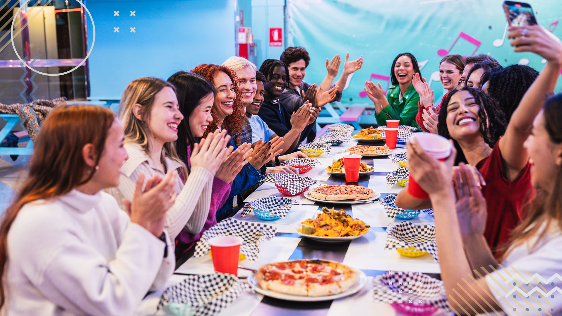 Happy team of colleagues celebrating the end of season gathered at a long table with pizza and nachos.